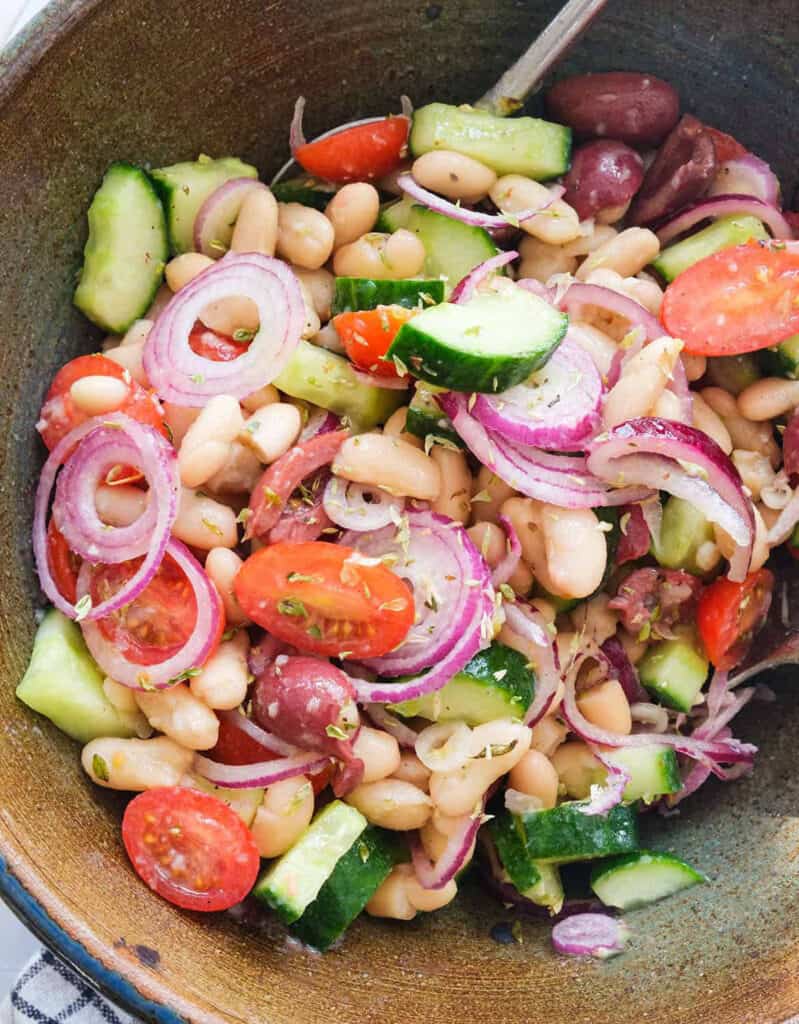 Top view of a brown salad bowl full of white bean salad with tomatoes and red onions.