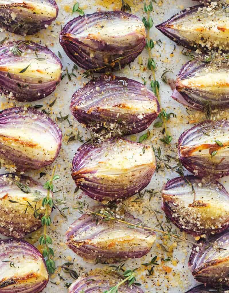 Top view of roasted onions with thyme and breadcrumbs over a white background.