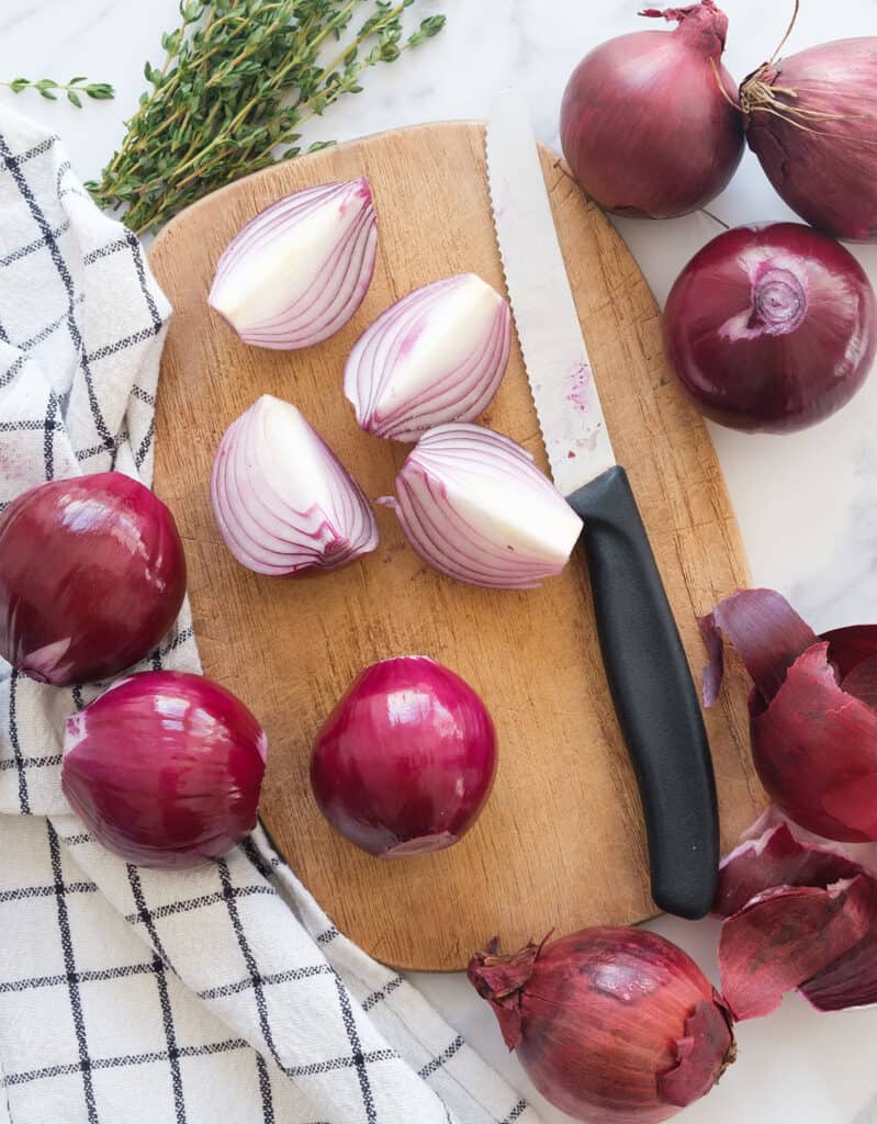 Top view of a chopping board with red onions cut into wedges.