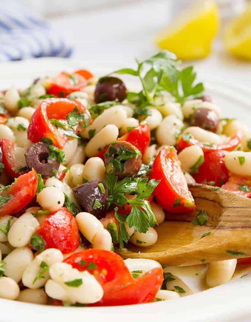 Close-up of a tray full of white bean salad with black olive and tomatoes.