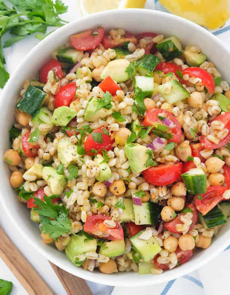 Top view of a white bowl full of barley salad with chickpeas and cherry tomatoes.