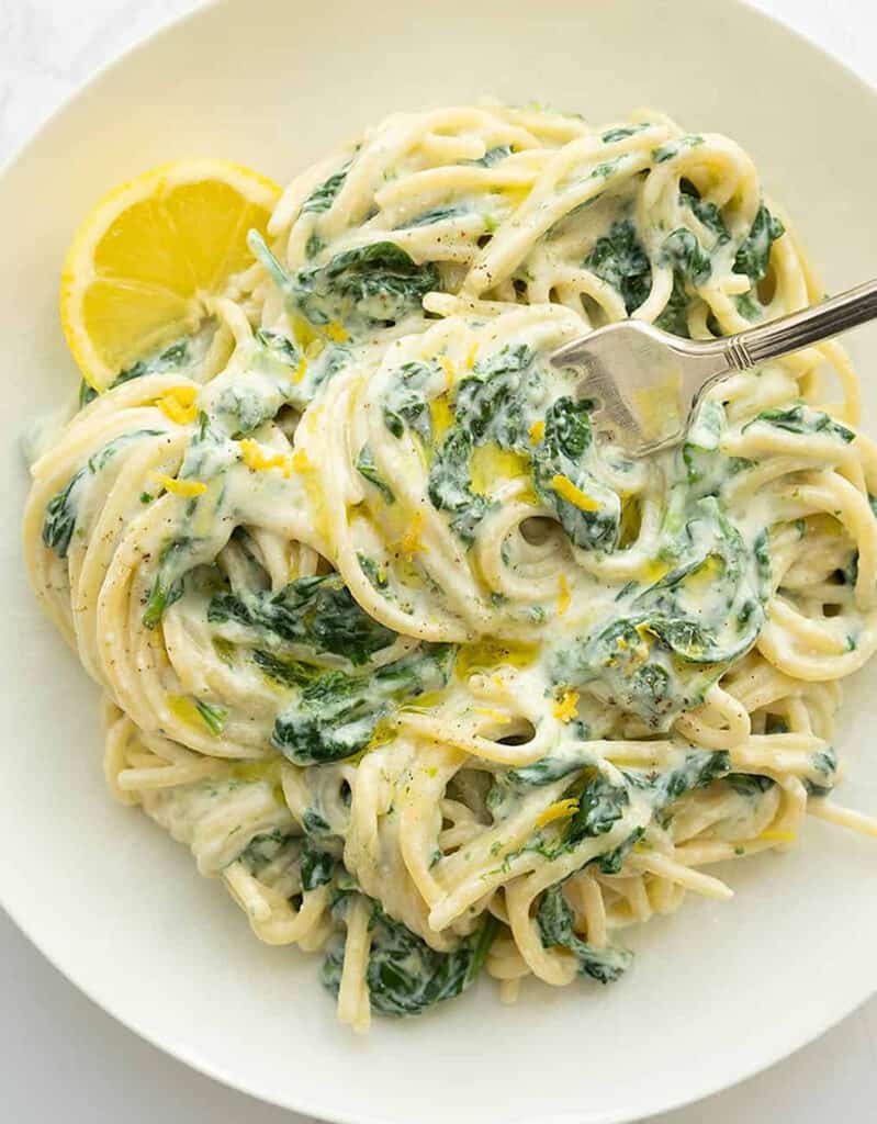 Top view of a white plate full of meatless spaghetti with ricotta, spinach and lemon zest.