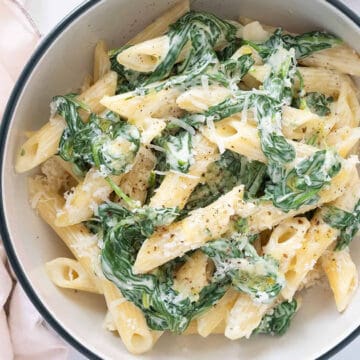 Top view of a bowl full of penne pasta with spinach.
