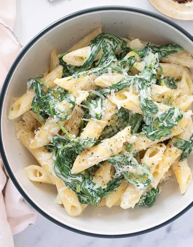 Top view of a white bowl full of meatless penne pasta with spinach and parmesan.