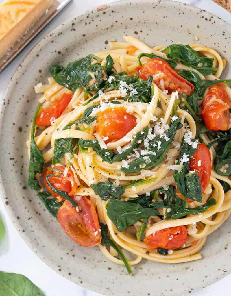 Top view of a grey plate full of meatless spaghetti with spinach and cherry tomato sauce.