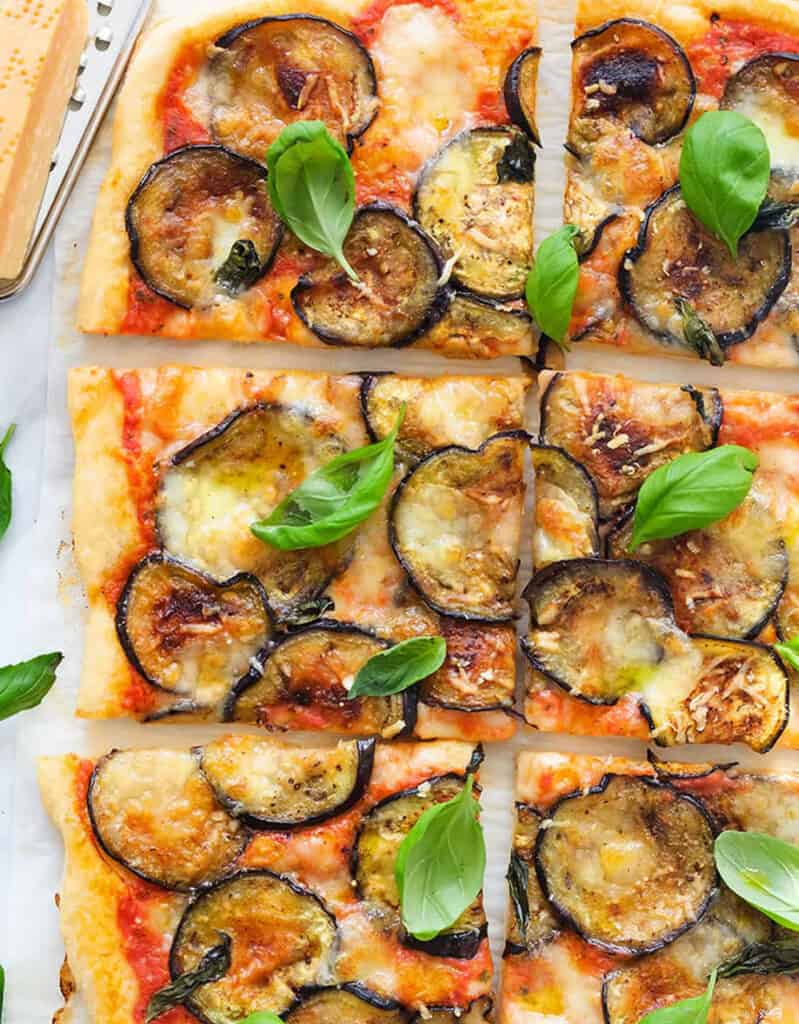 Top view of a large pizza with eggplant slices and fresh basil.