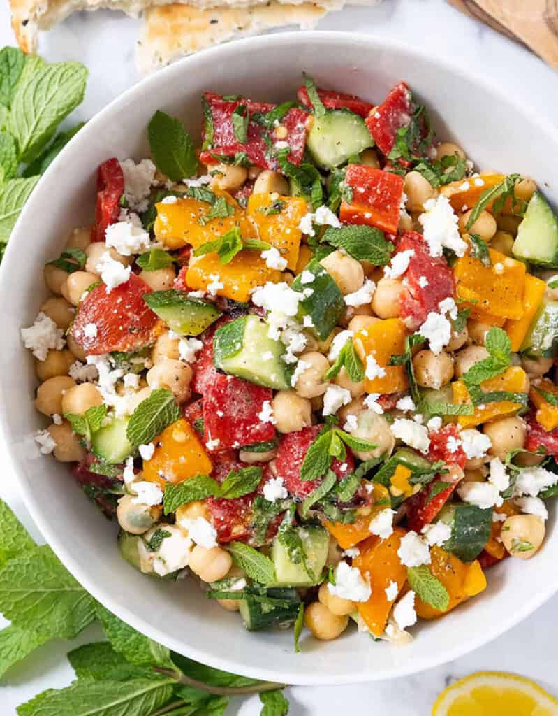 Top view of a white bowl full of chickpea salad with peppers, mint and feta cheese.