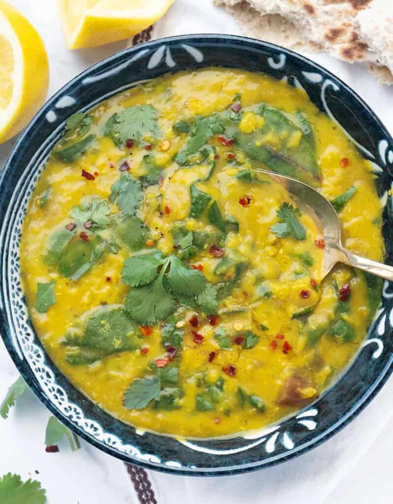 Top view of a darl bowl full of vibrant red lentil soup with swiss chard and cilantro.