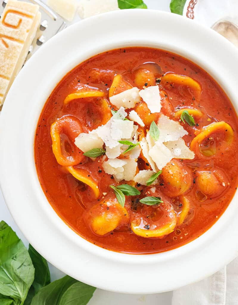 Top view of a white bowl full of tomato soup with orecchiette and shaved parmesan cheese.