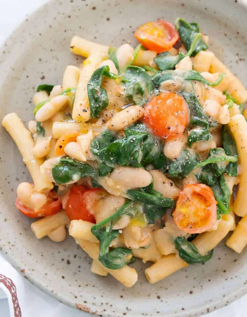 Top view of a grey plate with pasta with white beans, tomatoes and spinach, one of my fav meatless recipes.