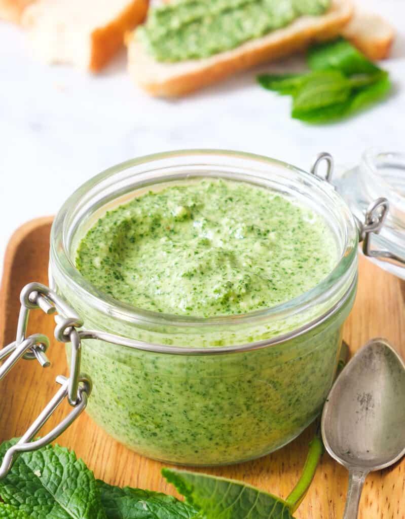 Close-up of a glass jar full of mint pesto with crusty bread in the background.