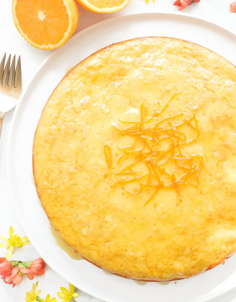하얀 접시에 둥근 빛나는 오렌지 케이크의 꼭대기 전망이 제공됩니다.