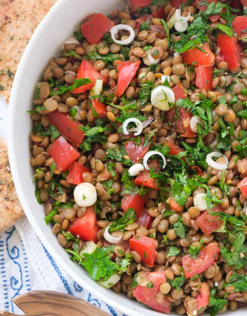 Top view of a white bowl full of lentil tabbouleh, diced tomatoes and fresh parsley.