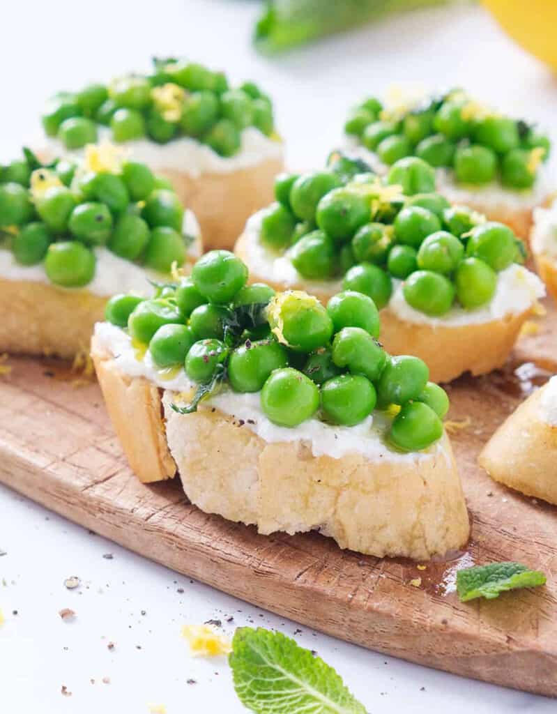 Crostini with peas, ricotta and mint served over a small wooden board.