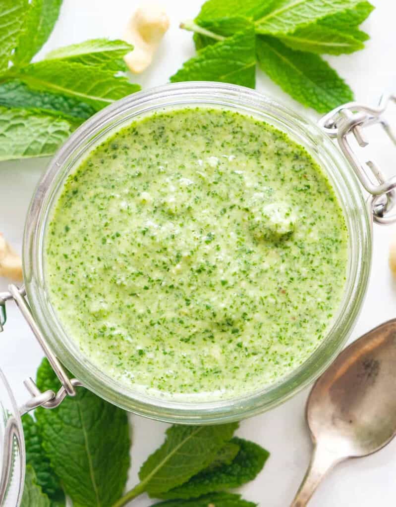 Top view of a glass jar full of mint pesto and fresh mint leaves in the background.