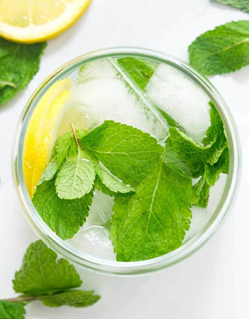 Top view of a glass full of mint water and ice over a white background.