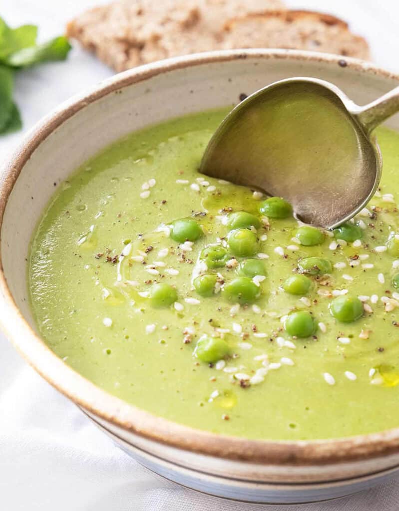 Close-up of a rustic bowl full of pea soup with mint garnished with sesame seeds.