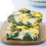Close-up of two slices of spinach frittata served on a small wooden board.