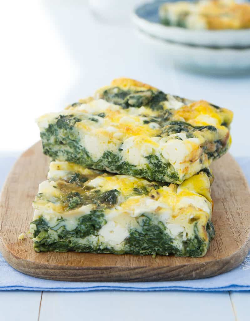 Close-up of two slices of spinach frittata served on a small wooden board.