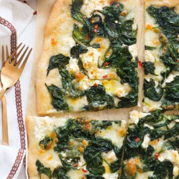 Top view of a large spinach pizza cut into slices.