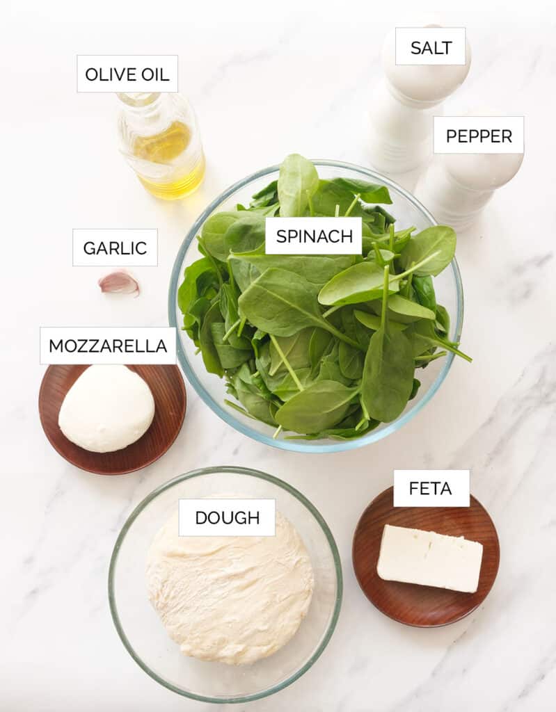 The ingredients to make this spinach pizza are arranged over a white background.