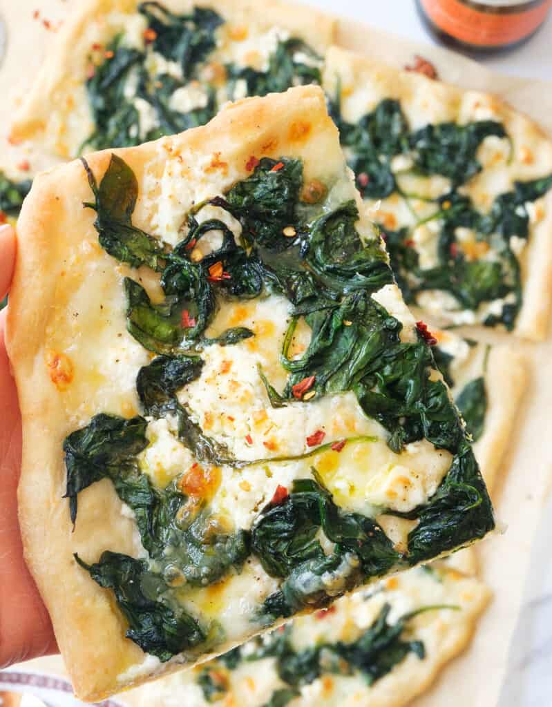 Close-up of a slice of spinach pizza drizzle with extra virgin olive oil.