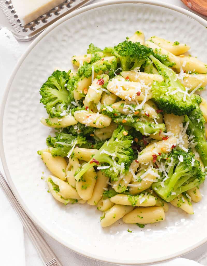 Top view of a white plate full of cavatelli and broccoli served with grated pecorino cheese.