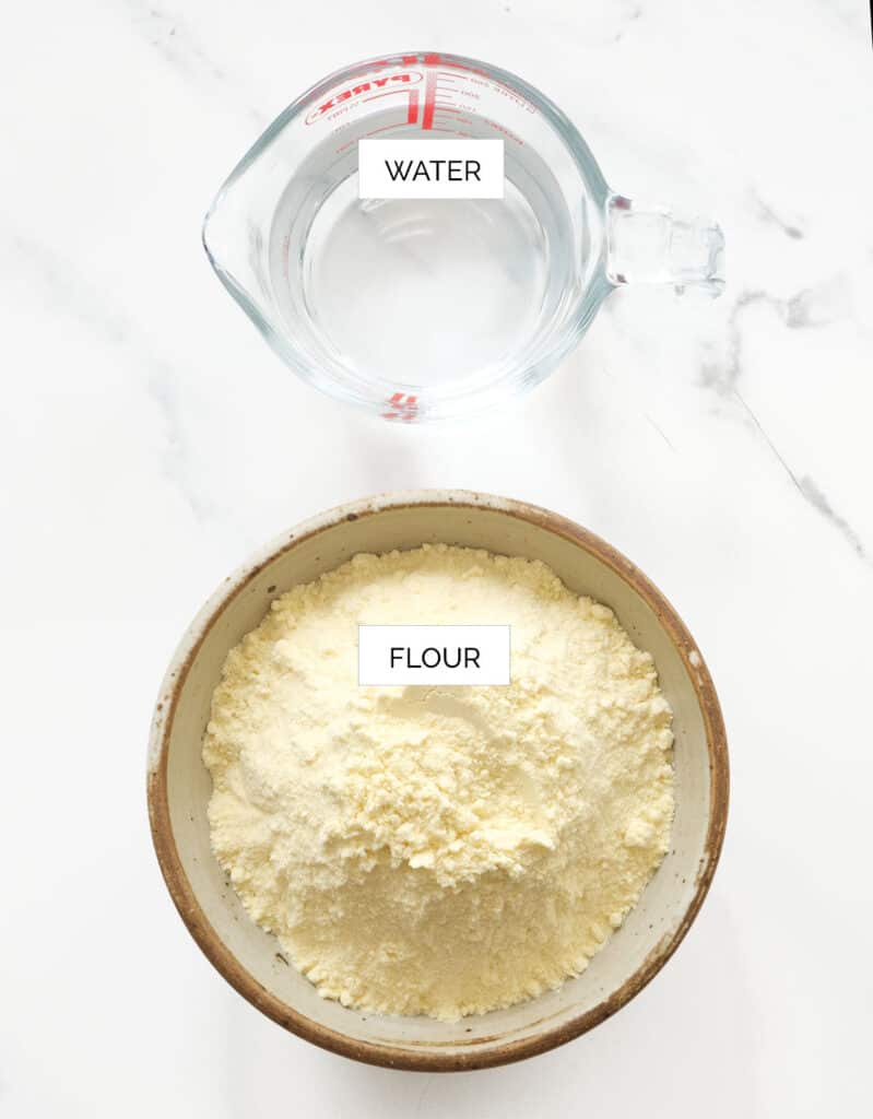 Top view of a bowl full of flour and a glass jug containing water.