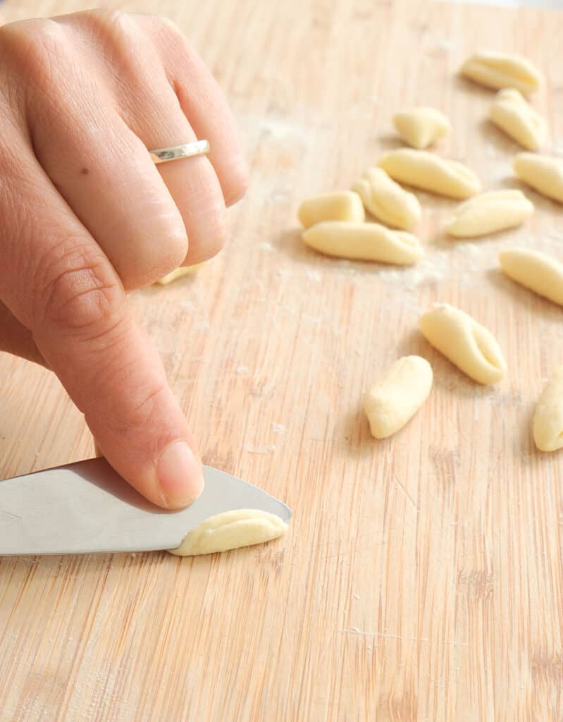 Close-up of two hands and a knife showing how to shape cavatelli pasta.
