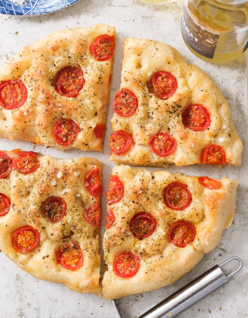Top view of a large round focaccia with tomatoes and oregano over a white background.