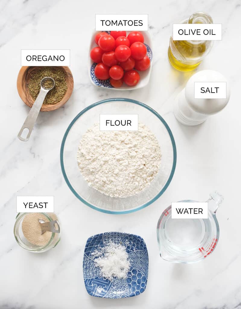 The ingredients to make this focaccia with tomatoes are arranged over a white background.
