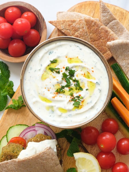 Top view of a bowl full of creamy mint yogurt sauce served with pita bread, falafels, cherry tomatoes and veggie sticks.