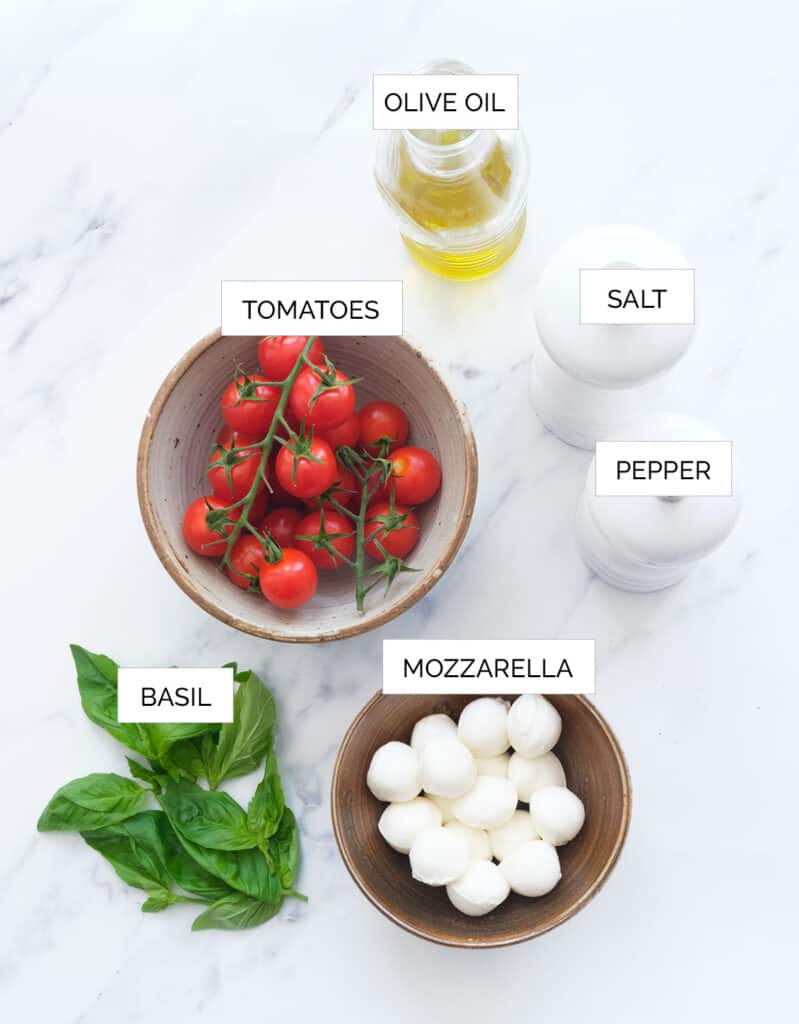The ingredients to make the caprese salad skewers are arranged over a white background.