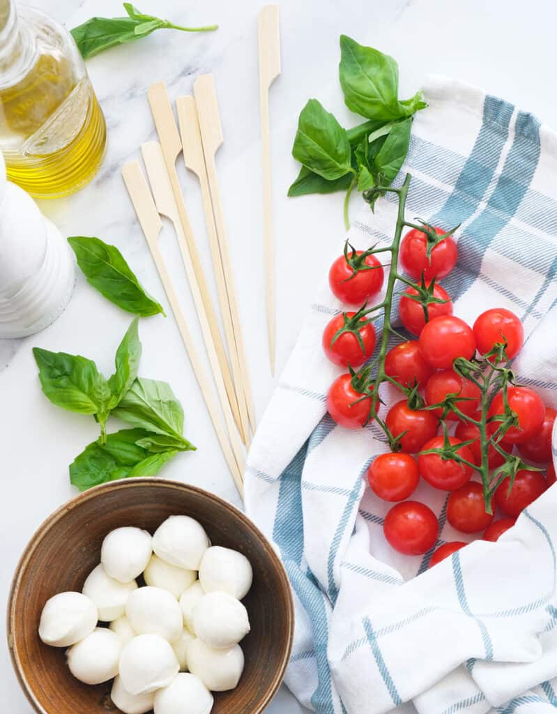 Top view of cherry tomatoes, baby mozzarella, basil leaves and wooden skewers.