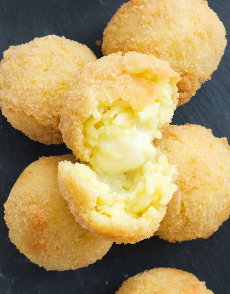 Close-up of fried arancini on a black background showing the molten mozzarella.
