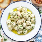 Top view of a white plate full of marinated mozzarella balls with olive oil and herbs.