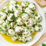 Top view of a white plate full of marinated mozzarella balls with olive oil and herbs.