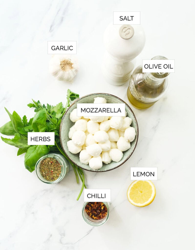 The ingredients to make marinated mozzarella balls are arranged over a white backgroun