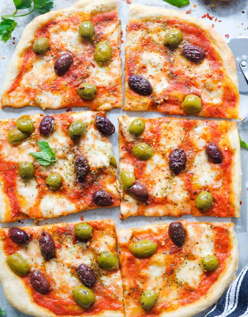 Top view of a large scrumptious olive pizza cut into slices.