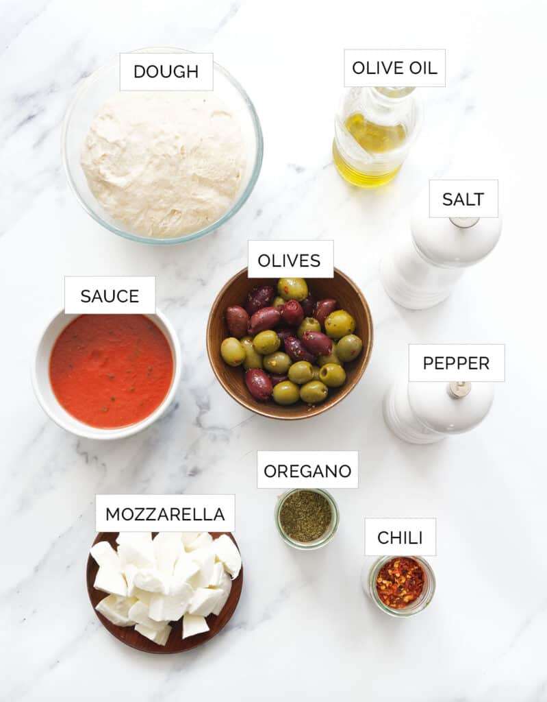 The ingredients to make this olive pizza are arranged over a white background.