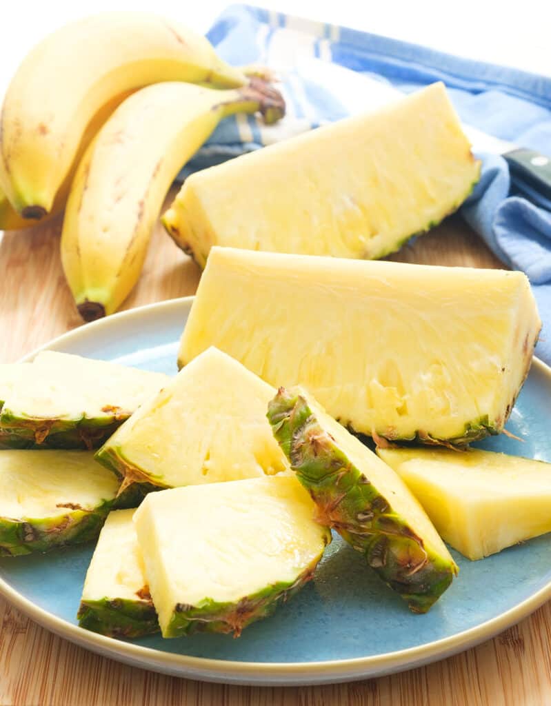 Close-up of a fresh pineapple cut into slices and a few bananas in the background.
