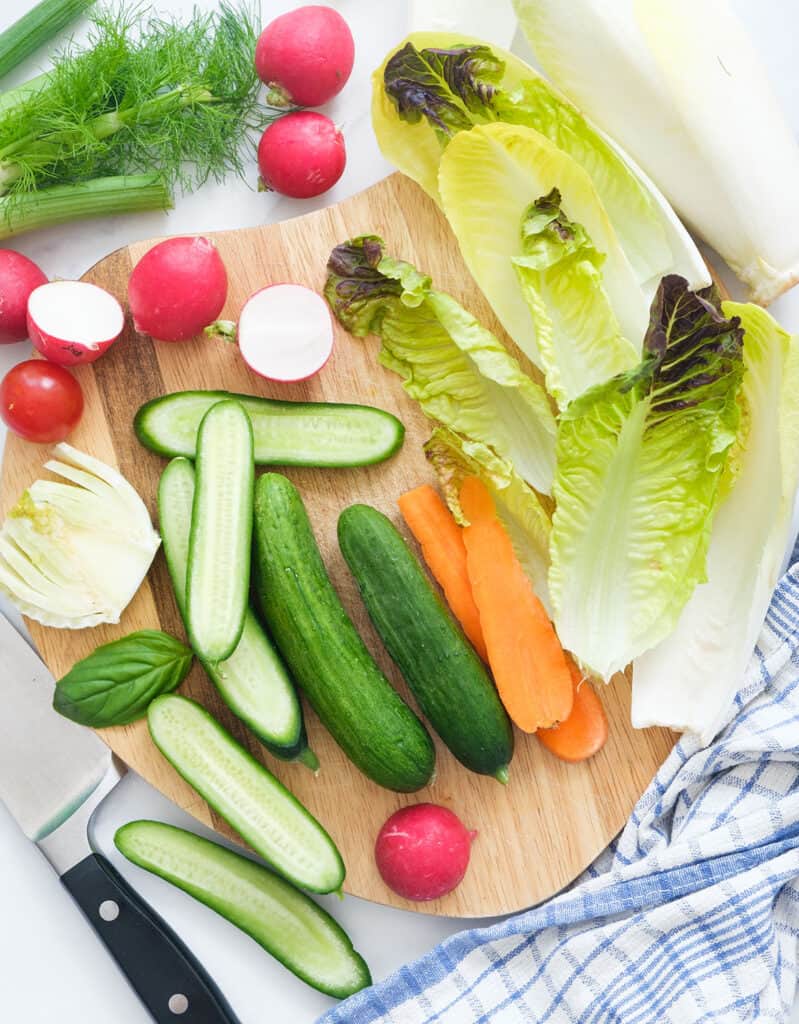 Top view of crisp, fresh cucumber, radish, carrots and salad leaves on a wooden board.