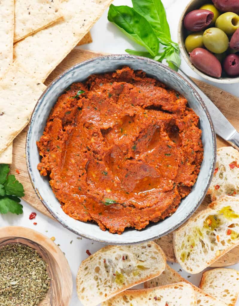 Top view of a bowl full of sun dried tomato paste served with crusty bread and crackers.