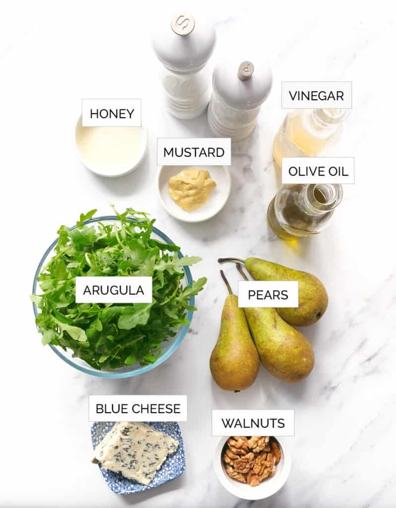 The ingredients to make this arugula pear salad are arranged over a white background.