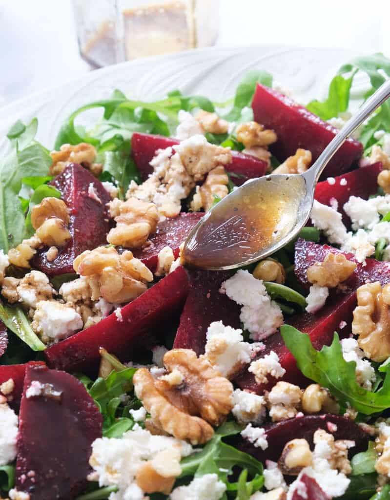 Close-up of a spoon pouring the salad dressing over the beets and the arugula leaves.