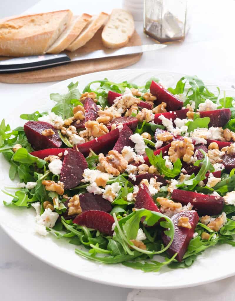 A large serving plate full of beet salad with arugula, feta and watnuts.