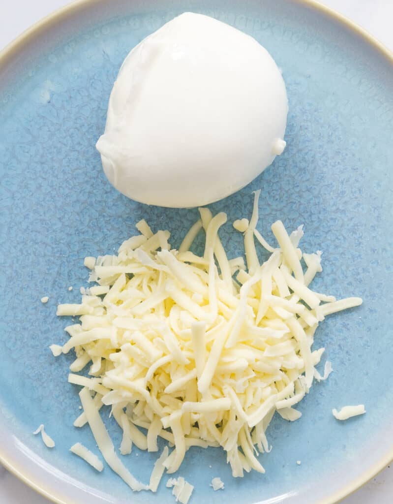 Top view of a fresh mozzarella ball and shredded mozzarella on a blue plate.