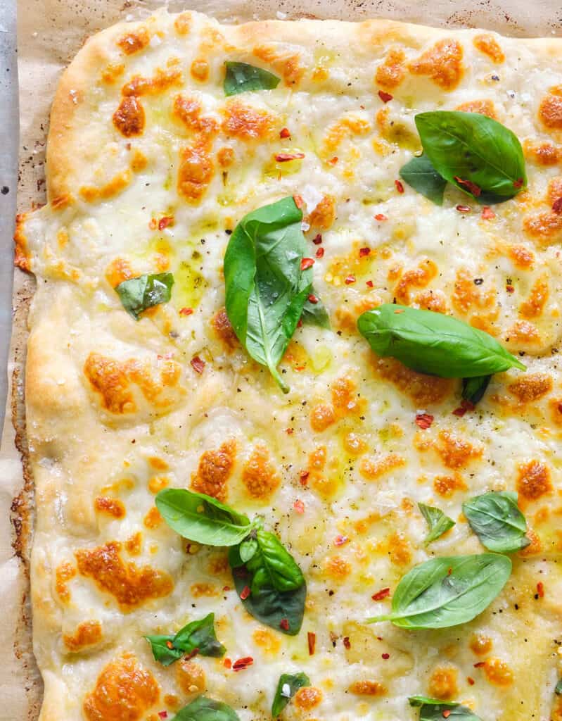 녹은 치즈와 신선한 바질 잎을 보여주는 모짜렐라 피자 부분의 클로즈업.