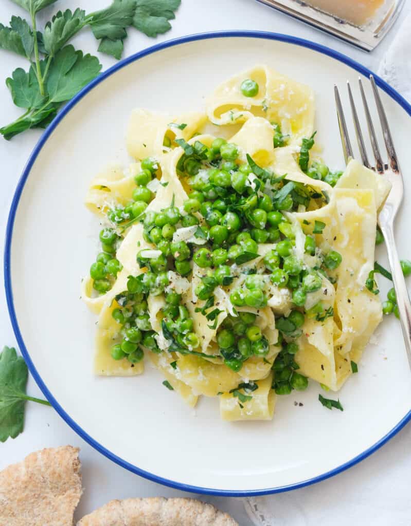 Top view of a white plate full of pappardelle pasta with peas and parmesan.