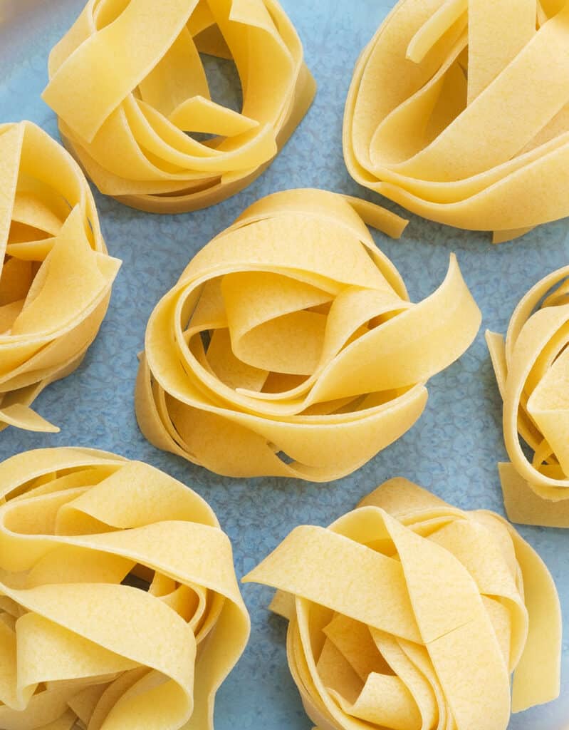 Top view of a few nests of pappardelle strands on a blue plate.